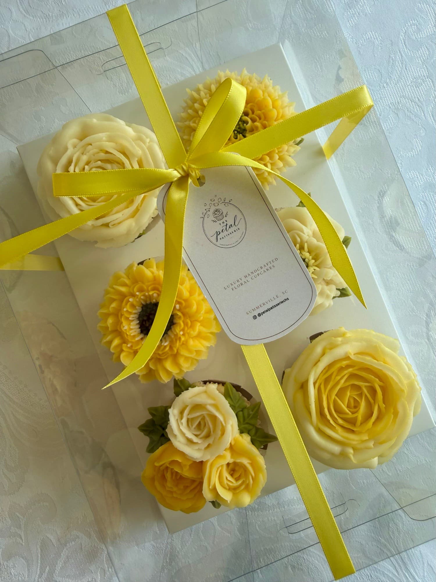 Yellow and cream floral cupcakes in a clear gift box tied with yellow ribbon
