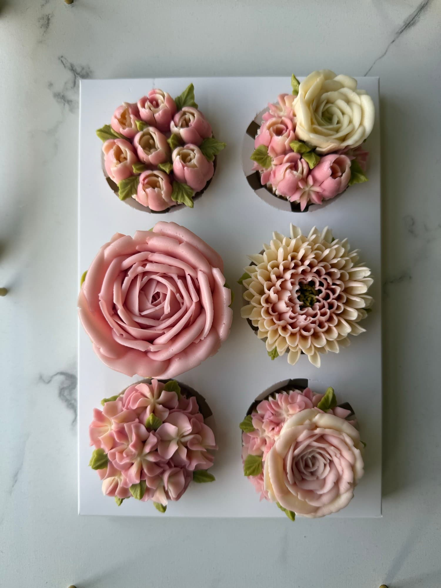 Six blush pink and ivory floral cupcakes on a white board over marble